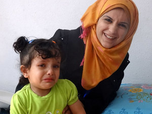 JVCが実施中の「子どもたちの栄養失調予防事業」で働くボランティア女性（右）と、貧血検査を怖がって泣く女の子。ガザ地区中部のジャバリヤ市にて。<br/>(2014年5月20日)今野撮影