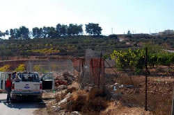 村の中（手前）から道路につながる道にはゲートが設置されている。道路の向こう側の畑の上方には入植地が見える