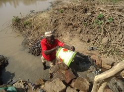 池につかりながら水汲みをするティヤさん。普段はジャラビーヤと呼ばれる白いガウンを着ていることが多いが、この日は完全に作業モード