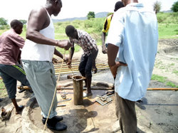 パイプを抜いた後、井戸内部に垂らしたヒモで水深を測り、十分な水量があるかどうかを確かめる。アルヌール技師、暑いらしく長袖シャツを脱いでランニング姿。