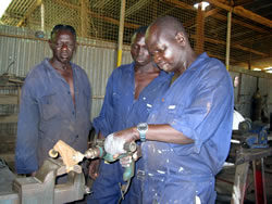 電動ドリルの使い方を研修生に見せるサミュエルさん（右）と、見つめるエウィコ（中央）