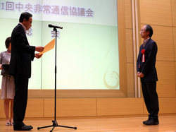 表彰状を受け取る現地調整員の楢崎知行（男性壇上）