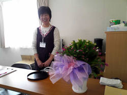 新しく採用された鎌田さんとお祝いのお花（紅白の花が咲くしゃこサボテン。仮設住宅近くの復興商店街にある