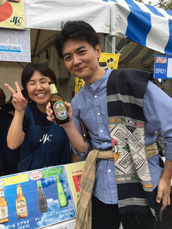 JVCが出展していたイベントでの石川と小河原さん。小河原さんの手にはラオスビール、肩にはラオスの素敵な布地が！